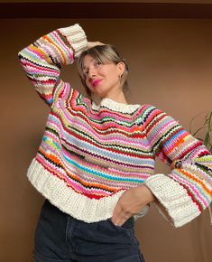 a woman wearing a multicolored knit sweater and jeans with her hands on her head