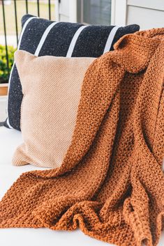 an orange knitted blanket sitting on top of a bed next to pillows and a pillow