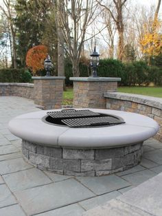 a fire pit sitting on top of a stone patio next to a wall and trees