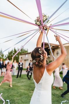 a woman in a white dress is holding up a pink ribbon over her head while other people are dancing behind her