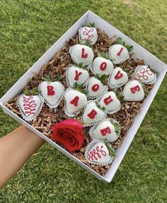 a box filled with lots of white chocolates on top of grass next to a red rose