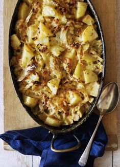 a casserole dish with potatoes and meat in it on a wooden table next to a blue napkin