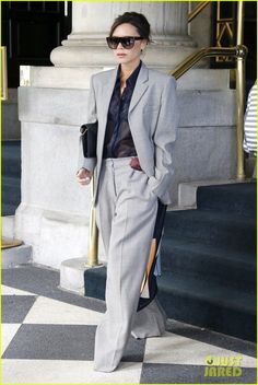 a woman in grey suit and sunglasses is walking down the street with her hand on her hip