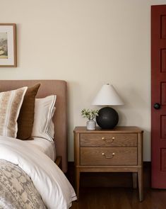 a bed sitting next to a red door and a lamp on top of a wooden dresser