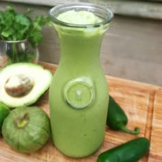 a green smoothie in a glass next to sliced avocado on a cutting board