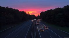 cars driving down the highway at sunset with trees in the background and traffic lights on both sides