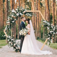 a bride and groom standing in front of an arch decorated with white flowers, greenery and foliage