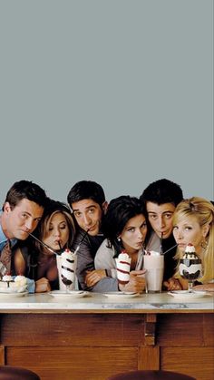 a group of people sitting at a table eating cake and drinking milkshakes in front of them