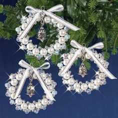 two christmas wreaths with bells and bows are hanging from a fir tree, surrounded by ornaments