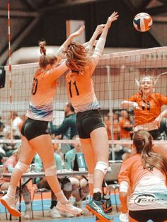 two female volleyball players jumping up to hit the ball