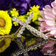 a close up of a cross on a chain with flowers in the backgroud