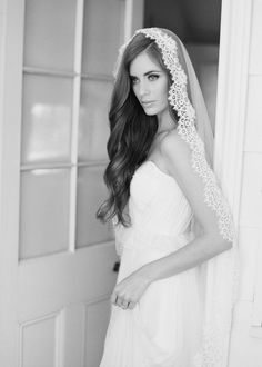 a woman in a wedding dress is standing near a door wearing a veil and looking at the camera