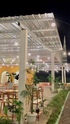 an outdoor dining area with tables and chairs under a white pergoline roof at night