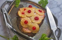 a piece of meat with pineapples and cherries is on a silver platter