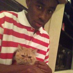 a man holding a cat in his arms while wearing a red and white striped shirt