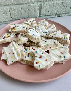 a pink plate topped with lots of white frosted cookies and sprinkles