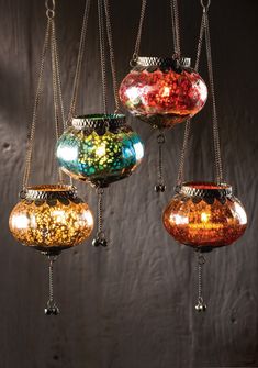 four glass vases hanging from chains in a room with dark wood wall behind them