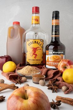 ingredients for apple cider cocktail displayed on white surface with apples, cinnamon and spices