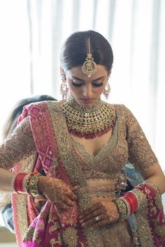 a woman in a red and gold bridal outfit looking down at her hands while wearing jewelry