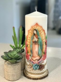 a lit candle with an image of the virgin mary on it next to a succulent plant