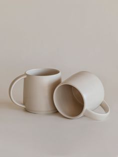 two white coffee mugs sitting next to each other on top of a gray surface