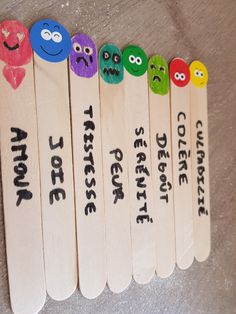 five wooden toothpicks with different colored faces and words on them, lined up in a row