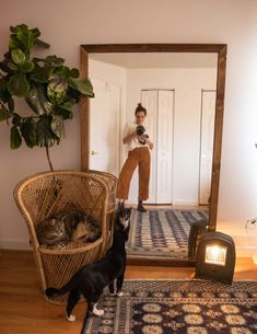 a woman taking a selfie in front of a mirror with her cat on the floor