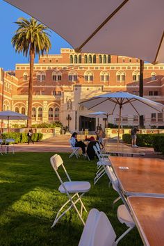 tables and chairs are set up under umbrellas in front of an old building with palm trees