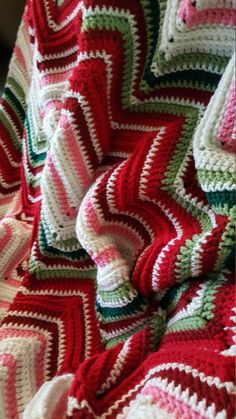 a crocheted blanket that is laying on top of a bed with red, green and white stripes