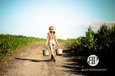 a woman walking down a dirt road carrying buckets