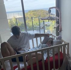 a woman sitting in a crib next to a baby and an adult looking at her phone