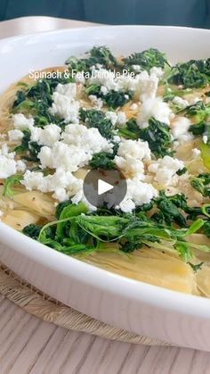 a white bowl filled with pasta and spinach covered in fettuccine, cheese and broccoli