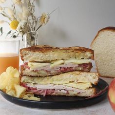 a sandwich cut in half sitting on top of a plate next to an apple and chips