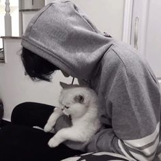 a person wearing a hoodie holding a white cat in their lap and looking at the camera