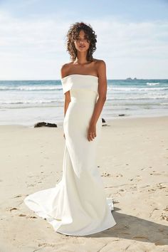 a woman standing on top of a sandy beach next to the ocean wearing a white dress