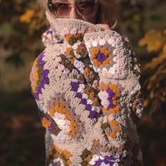 a woman wearing sunglasses covering her face with a crocheted blanket in the fall