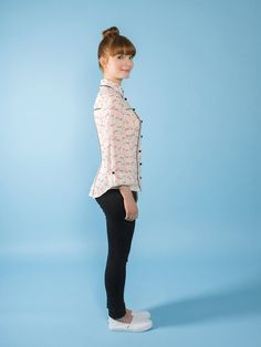 a woman standing in front of a blue background wearing black pants and a pink shirt