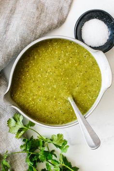 a white bowl filled with green soup next to some parsley