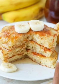 a stack of pancakes with bananas and syrup on a white plate next to some sliced bananas