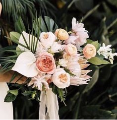 a bridal holding a bouquet of flowers in her hands with greenery behind it