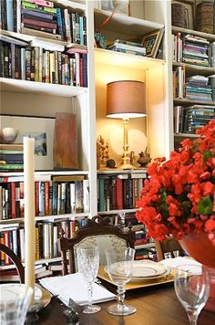 a dining room table is set with plates, glasses and flowers in front of bookshelves