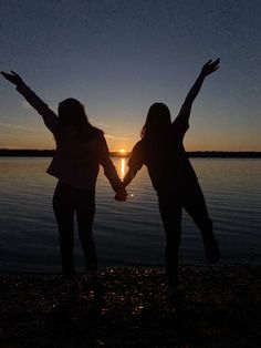 two girls holding hands while standing in front of the water