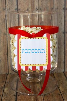 popcorn in a glass container with a red ribbon around the top and name on it