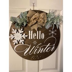 a wooden sign that says hello winter hanging on a door with snowflakes and greenery