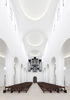 an empty church with rows of pews and organ pipes in the ceiling, all white