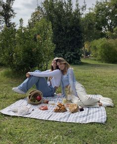 two women are sitting on a blanket in the grass and having a picnic with food