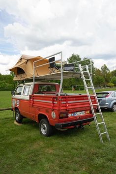 a red pick up truck parked on top of a lush green field next to a metal ladder