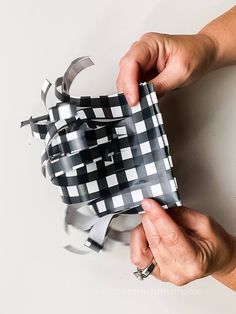 two hands holding a black and white checkered gift bag with silver ribbon on it