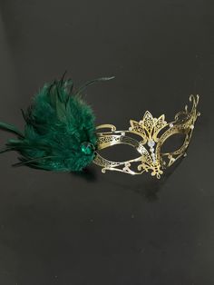 This mask is crafted in the tradition of Venetian masquerade, exuding timeless elegance and grace. The graceful green feathers add a touch of enchantment and create a mesmerizing aura around you. The sparkling emerald green stones accentuate the mask's design, illuminating your face with radiant brilliance. Whether you're attending a masquerade party, ball, or gala, this mask is the perfect choice! Age Group/Gender - Adult/Womens Size/Type - One size fits all adults Mask Color - Gold Rhinestone Color - Clear Mask Material - Metal Special Features - Green feathers Personalization - Not available Masquerade Mask Green And Gold, Emerald Green Masquerade Mask, Green Masks For Mardi Gras Carnival, Green Masquerade Mask For Mardi Gras Party, Green Masquerade Mask For Mardi Gras, Green Mask For Masquerade Carnival, Green Masks For Masquerade Carnival, Green Masks For Carnival Masquerade, Green Masks For Carnival Costume Party