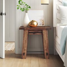 a bedroom with white walls and wood flooring has a small wooden table in front of the bed